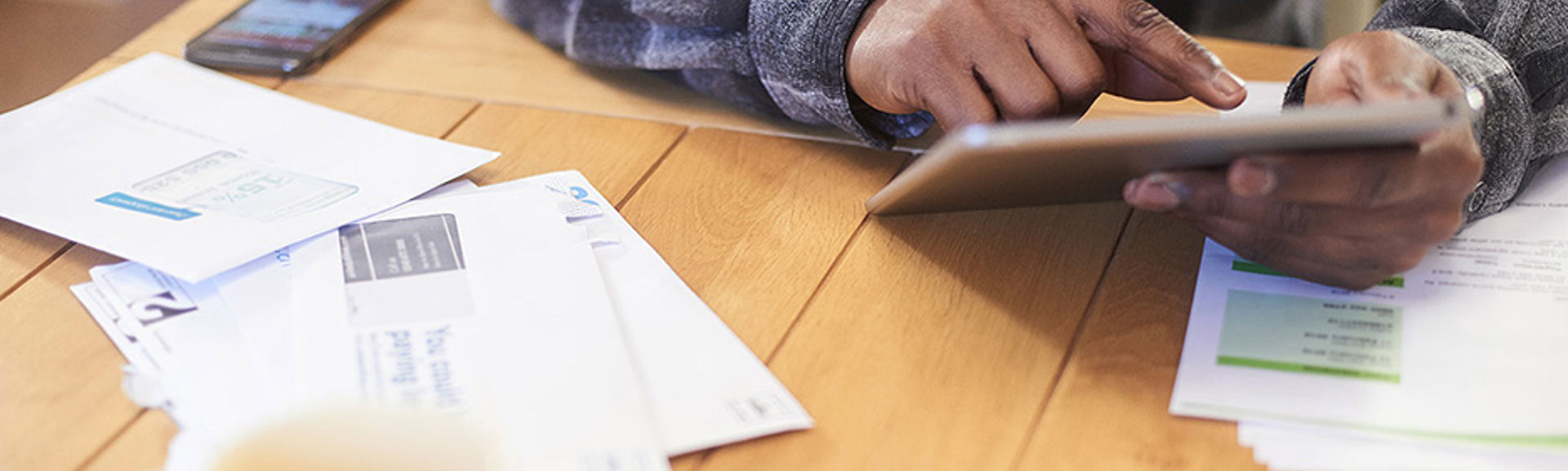 A man using a tablet at a table surrounded by paper bills