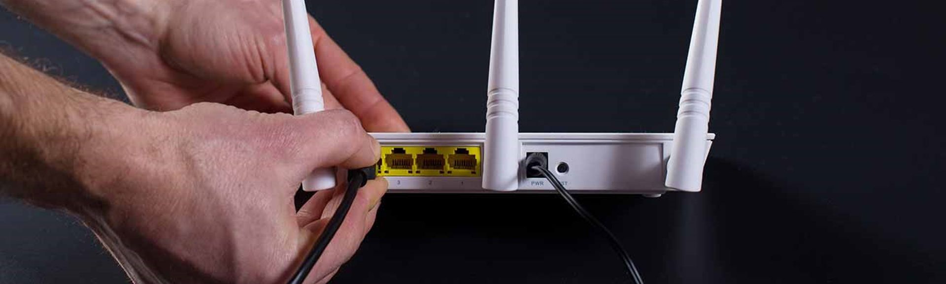 The back of a wireless broadband router with someone plugging-in an ethernet cable