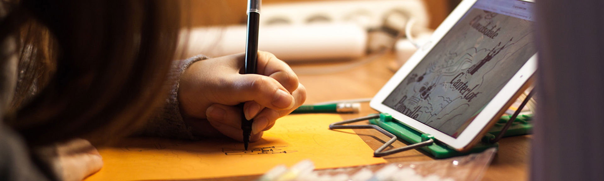 A girl making notes while following a lesson on a tablet device