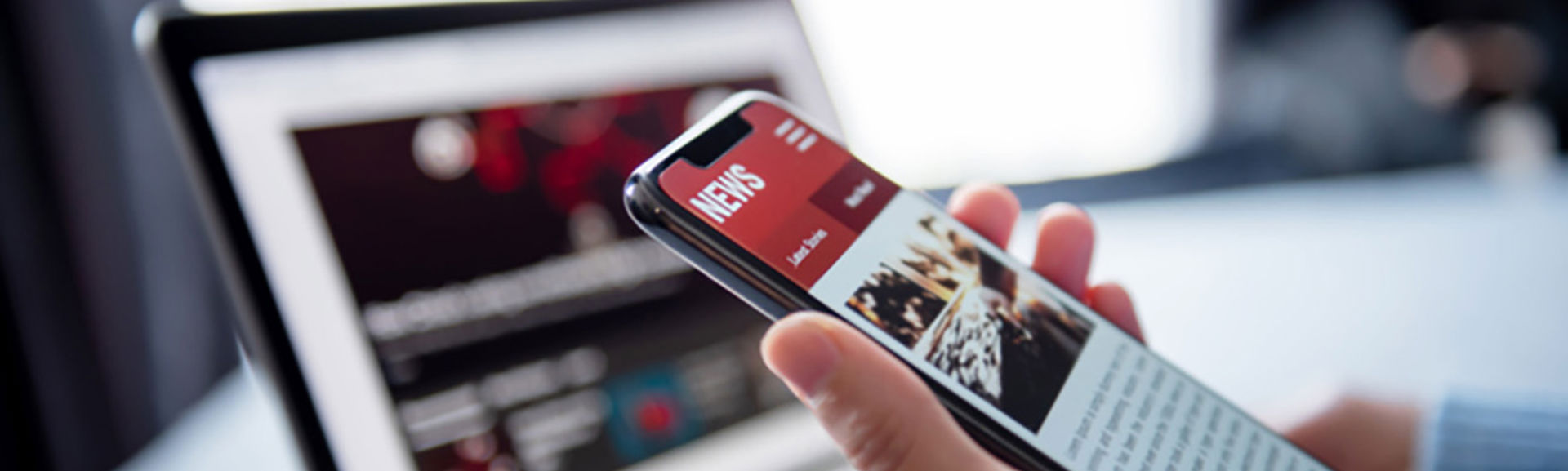 A person looking at news websites on their mobile phone and laptop
