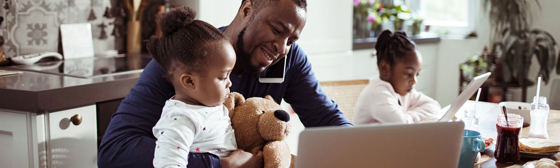 A family at breakfast using a number of devices including a laptop, tablet and a mobile phone