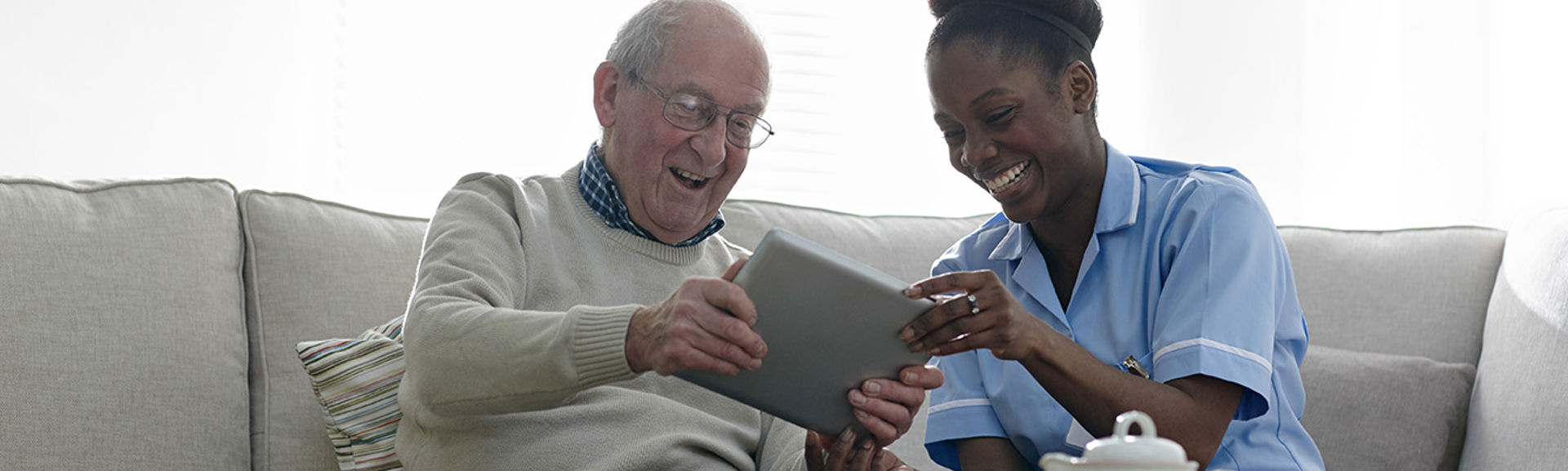 A nurse and elderly man using a tablet device together and smiling
