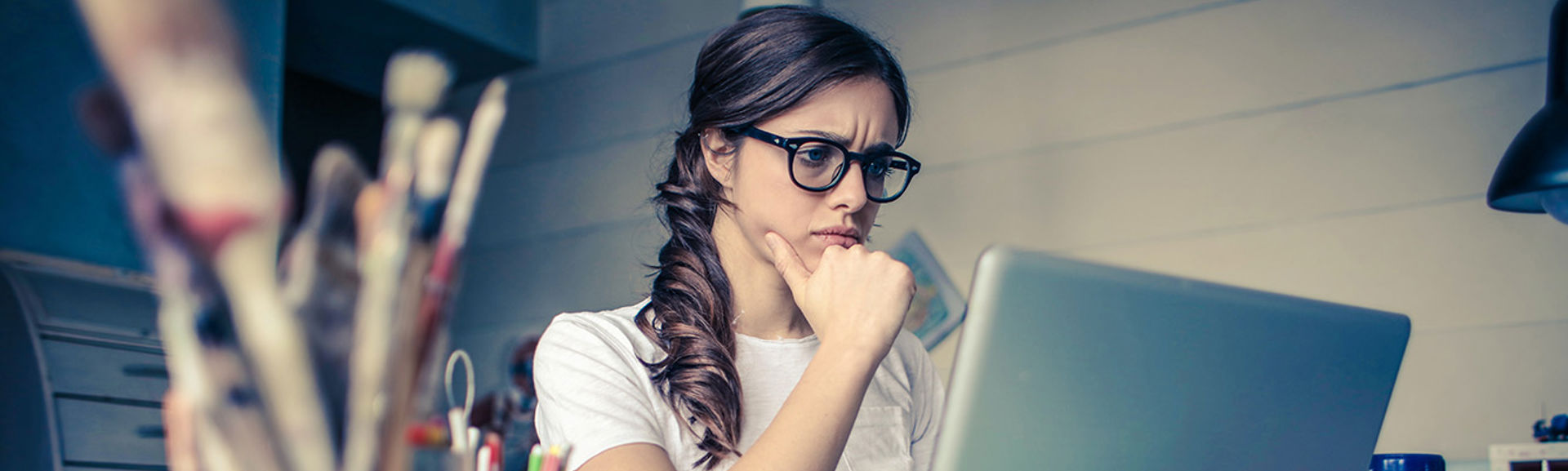 A young woman with a thoughtful expression looking at a laptop screen