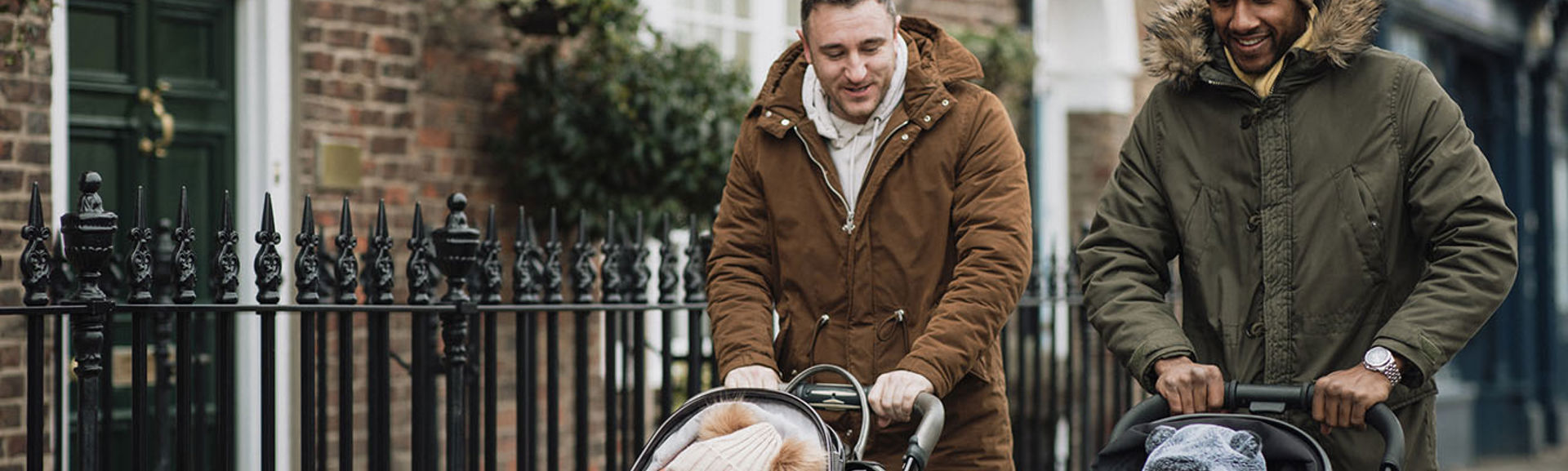 Two men walking along a road with babies in pushchairs