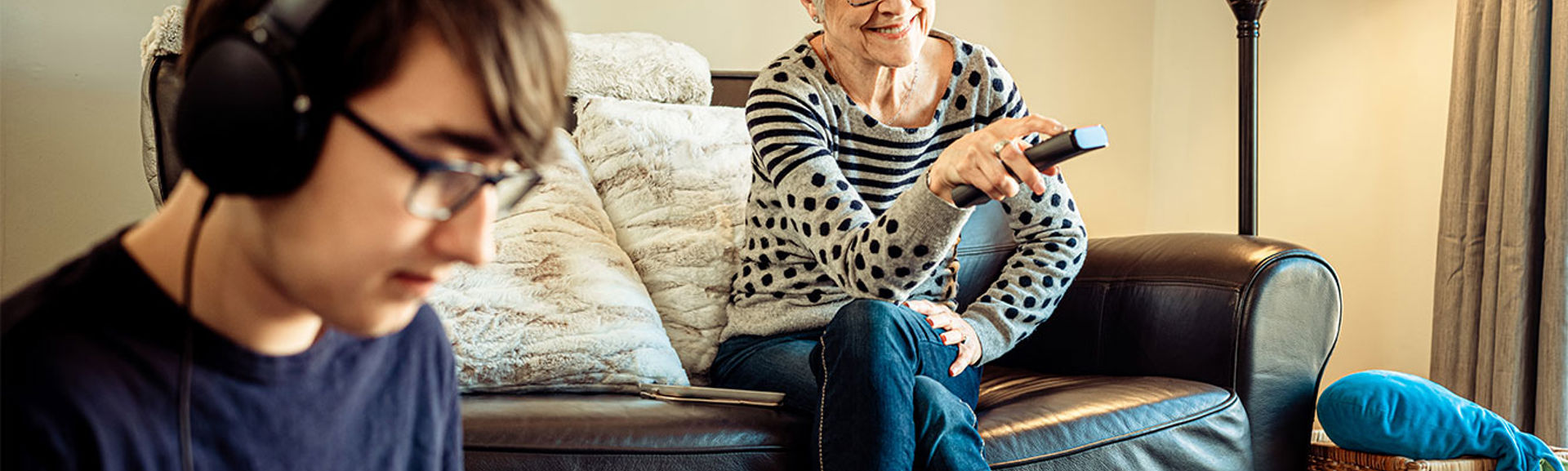 Elderly woman pressing a button on a TV remote, young man on his laptop