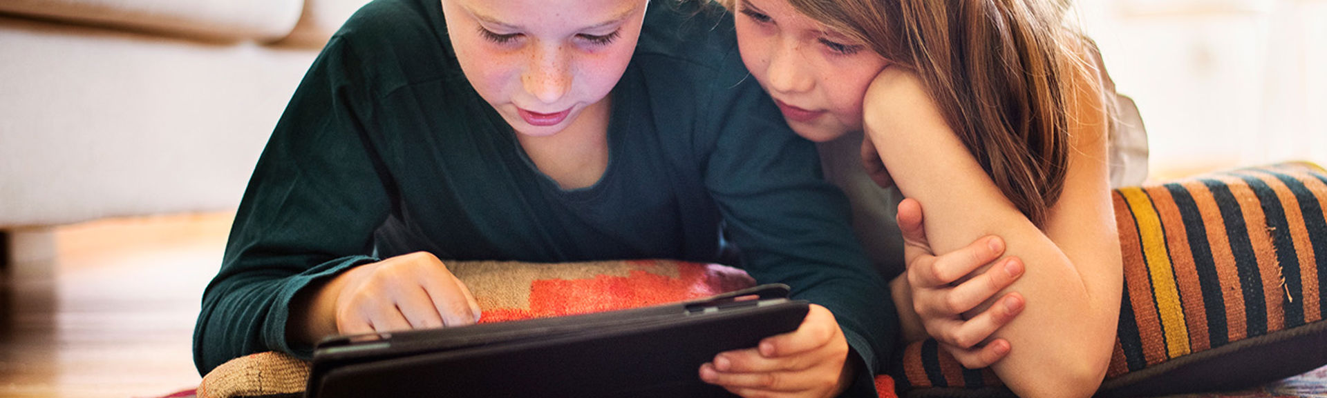 Brother and sister using tablet on living room floor