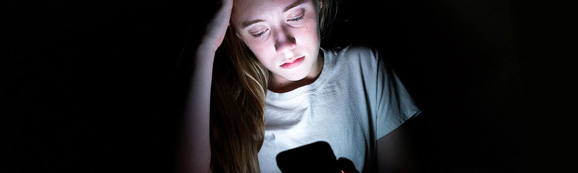 An unhappy girl using her mobile phone in a dark room
