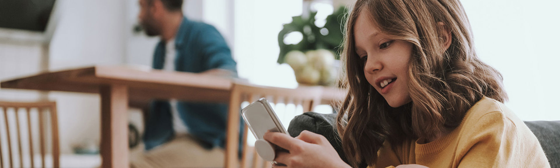 A girl happily looking at a mobile phone in a home environment