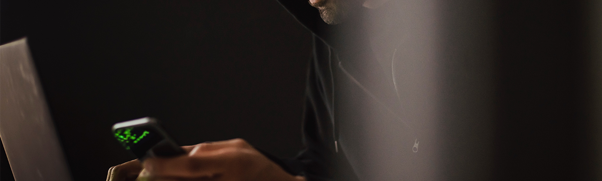 Man in a hoodie looking at phone in dark room