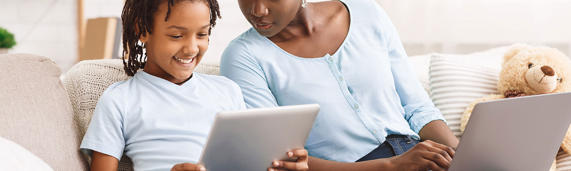 A woman working on a laptop sitting next to a young boy who is using a tablet device