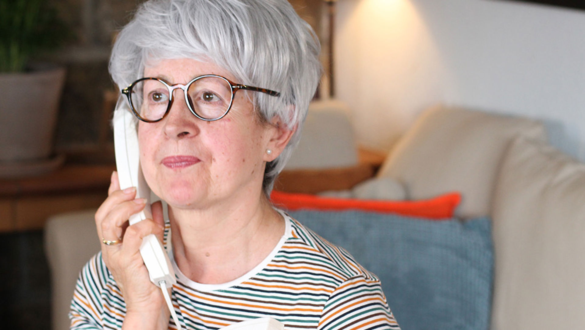 Elderly lady with a concerned look listening to a call on her home telephone
