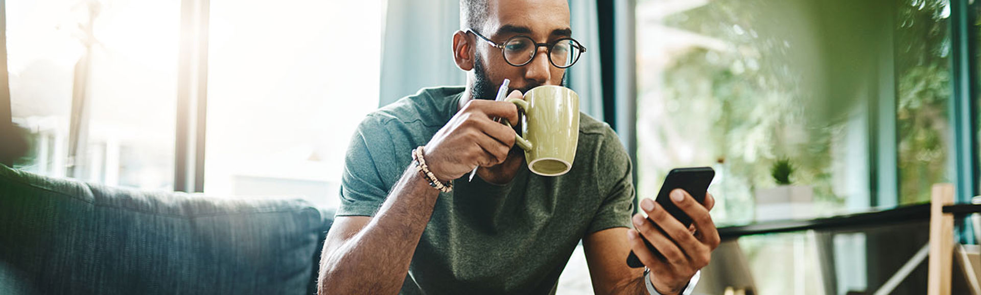 Man sitting on sofa drinking tea and looking at phone