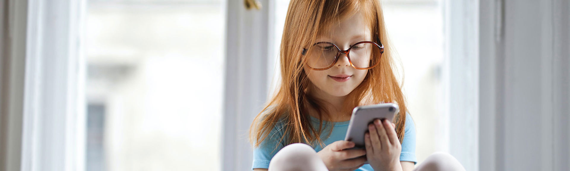 Young child wearing glasses, looking at a mobile phone