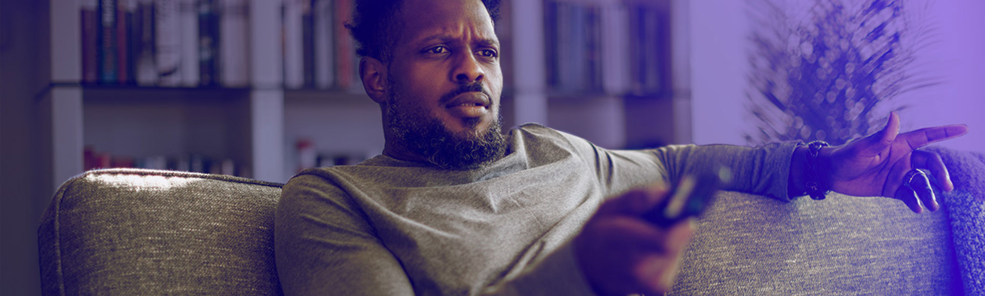 A man holding a television remote control and looking at the screen with a concerned expression