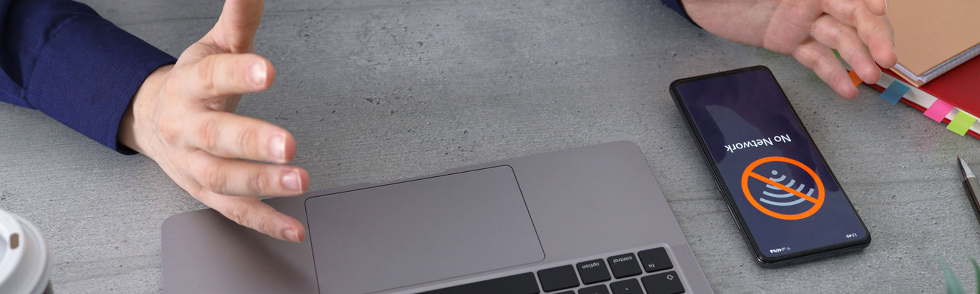 A person working at a laptop with a mobile phone next to it and a 'no network' message on screen