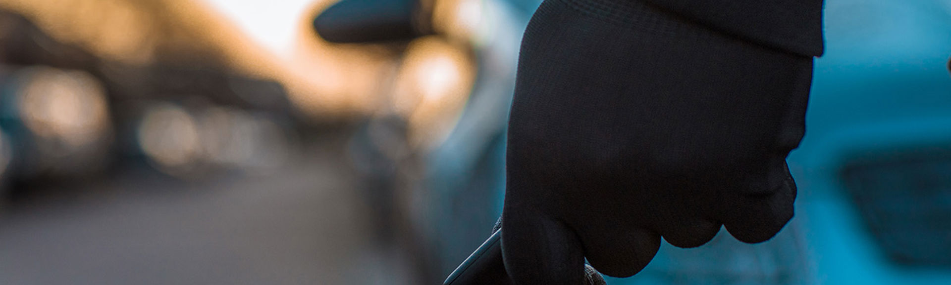 A shadowy hand holding a key fob in front of a car outside