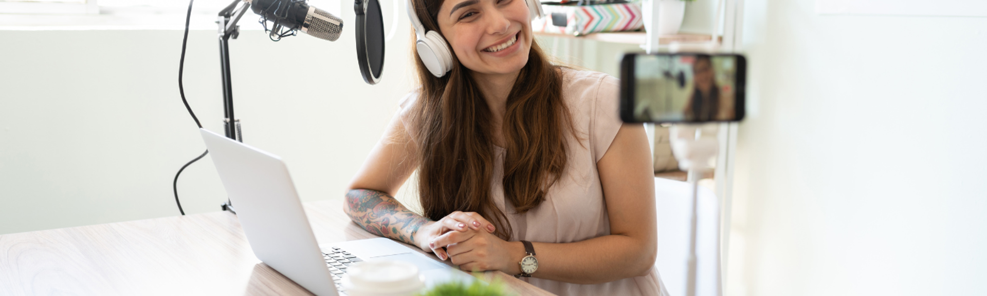 A woman wearing headphones filming herself in front of a microphone