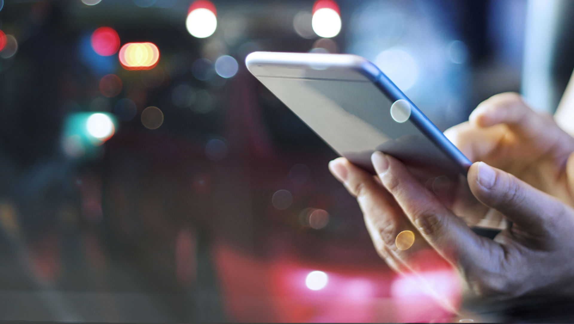 A person using a mobile phone with car headlights shown in the distance