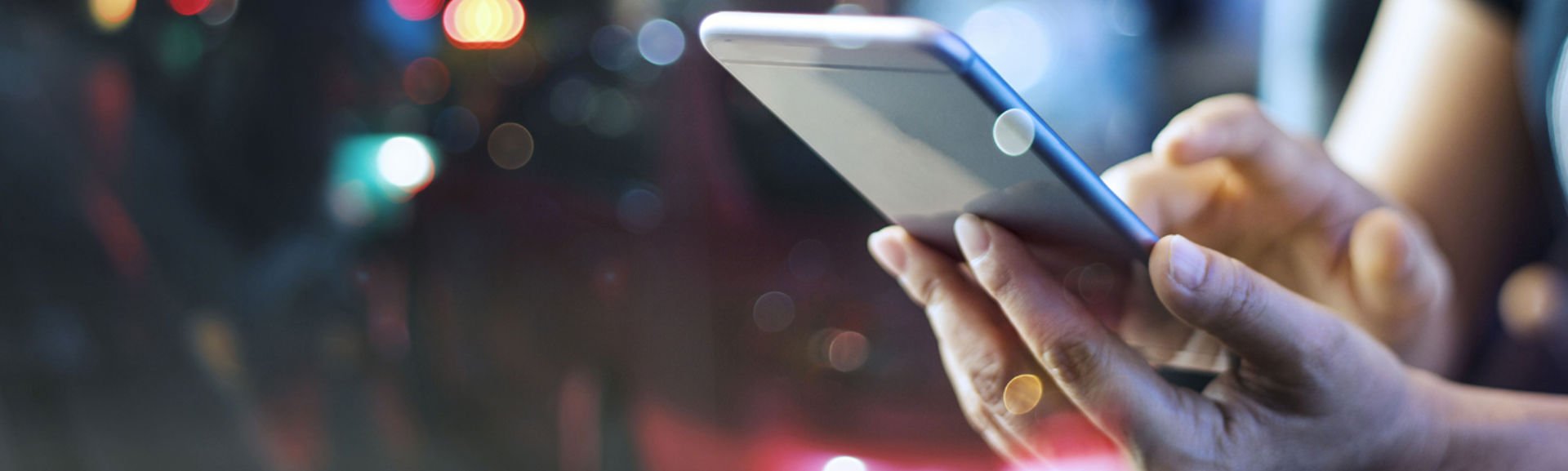A person using a mobile phone with car headlights shown in the distance