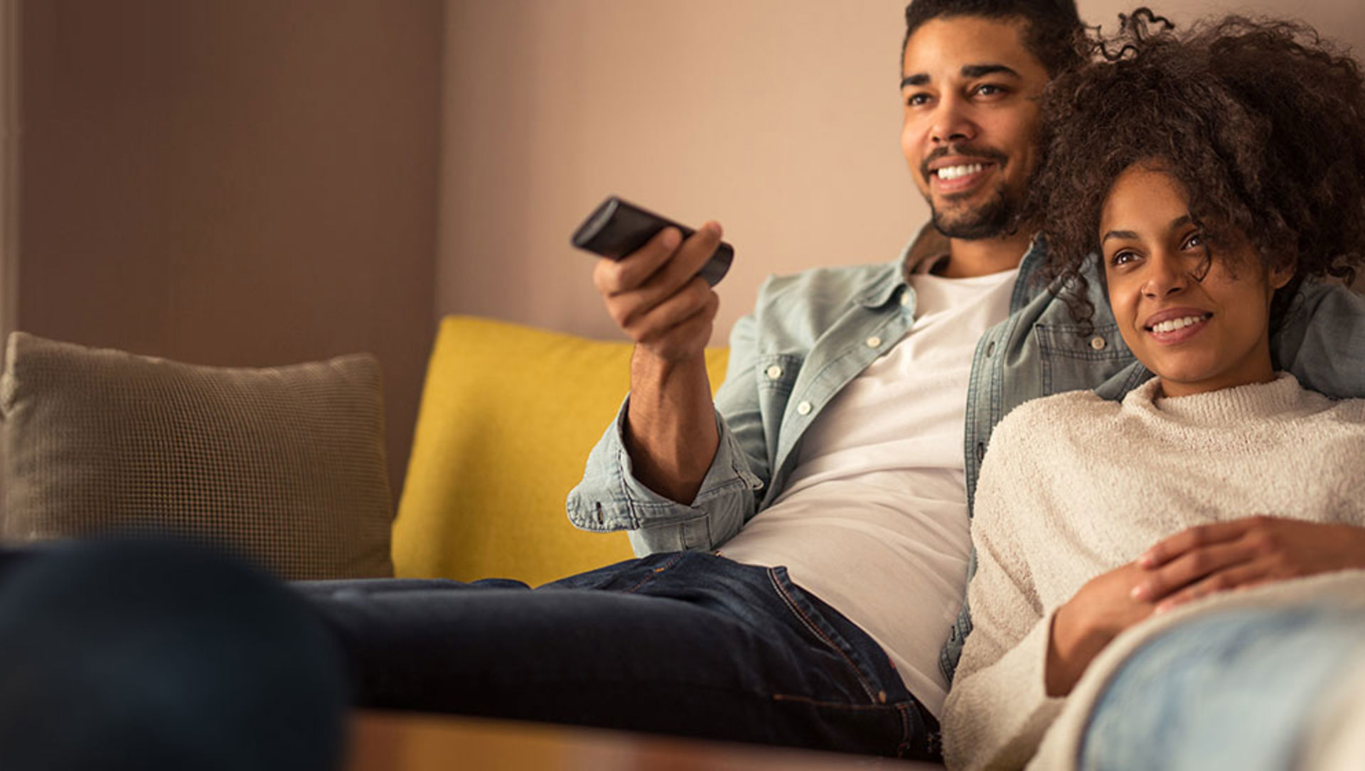 Couple on couch watching TV with a smart speaker in the foreground