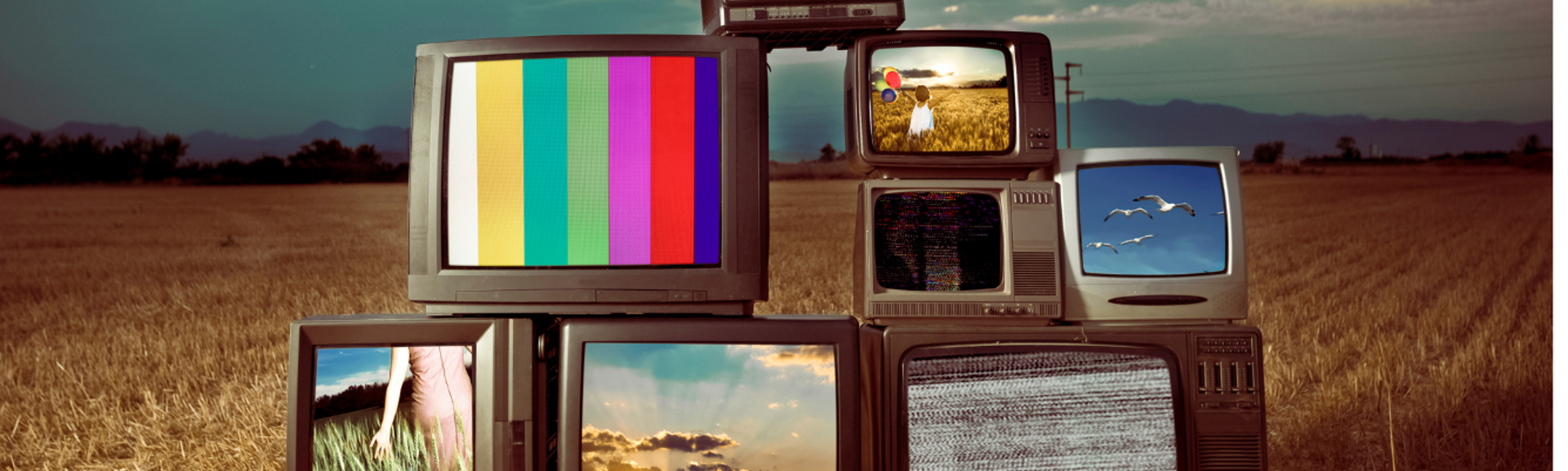 A collection of old television sets stacked in a pile but with screens working