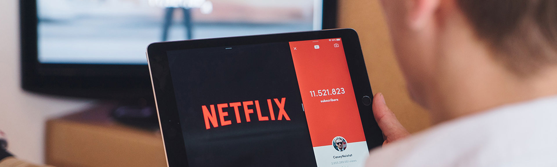 Person with Netflix on a tablet, with broadcast TV on in the background