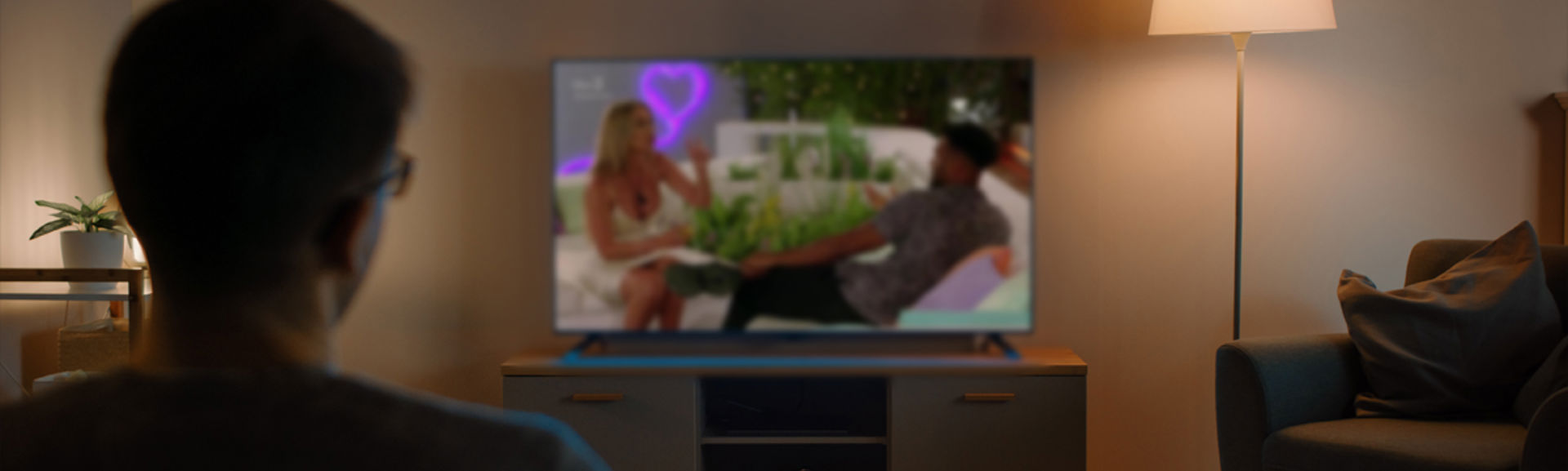 A person sitting on a sofa watching Love Island on their television